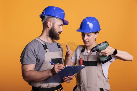 Photo for Engineers team looking at construction measurements on clipboard files, holding papers and power drill gun. Contractors talking about renovating project, preparing to work on refurbishment. - Royalty Free Image