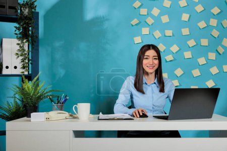 Téléchargez les photos : Optimiste asiatique spécialiste des ventes et du marketing féminin examinant les statistiques d'entreprise sur ordinateur portable. Professionnel assis au bureau travaillant sur les rapports pendant la journée de travail. - en image libre de droit