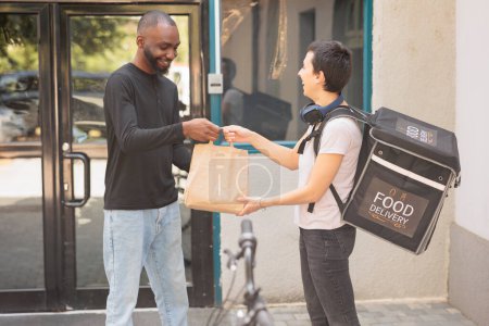 Photo for Express office food delivery service, courier giving client lunch paper bag. Smiling african american customer holding restaurant takeaway meal outdoors, woman with package - Royalty Free Image