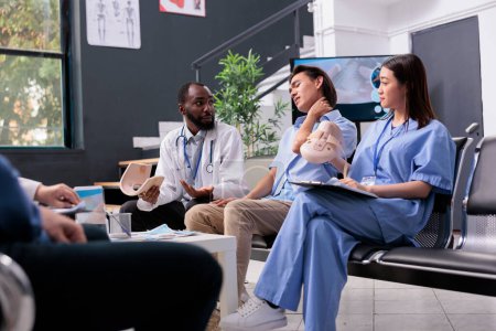 Photo for Medical staff removing cervical neck collar off of injured patient with fracture during consultation in hospital reception. Nurse and medic giving support to asian young man, health care service - Royalty Free Image