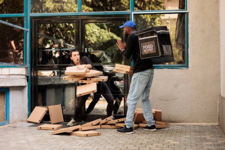 Téléchargez les photos : Femme confuse qui laisse tomber des boîtes à pizza, courrier effrayé regardant les paquets de repas à emporter tomber. Homme afro-américain négligent livrant fastfood, mauvais service de livraison - en image libre de droit