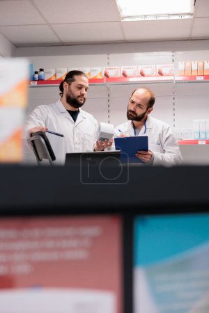 Photo for Caucasian colleagues standing at drugstore counter desk doing medication and pharmaceutical products inventory in pharmacy. Workers is trained to recognize and address any potential drug interactions - Royalty Free Image