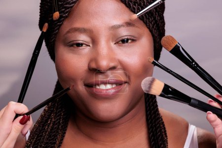 Photo for African american woman getting professional make up portrait. Makeup artists hands applying eye shadows and powder on model face, using decorative cosmetics brushes close up - Royalty Free Image