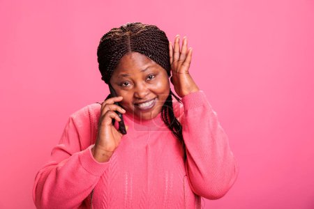 Photo for Happy joyful young adult smiling while having phone call conversation talking with remote friend on pink background. Cheerful african american model having fun, relaxing in studio - Royalty Free Image