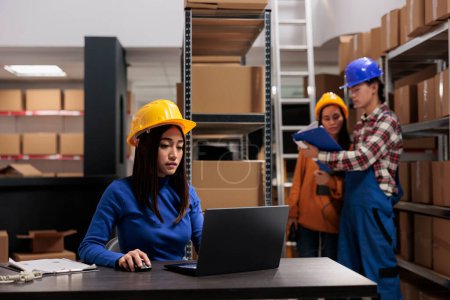 Photo for Retail storehouse young asian employee processing online order on laptop. Warehouse worker checking goods inventory automation system on computer in freight parcels storage room - Royalty Free Image
