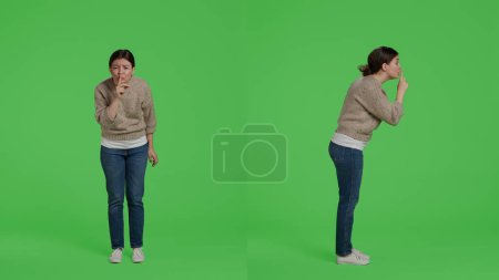Photo for Private person doing hush silence symbol to keep secret, showing mute gesture on camera over full body greenscreen. Woman expressing secrecy and confidential symbol in studio, privacy. - Royalty Free Image