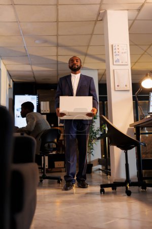 Photo for Dissapointed office worker packing personal belongings after being fired from corporate job. Depressed executive manager carrying cardboard box while leaving office late at night. Business concept - Royalty Free Image