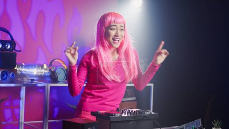 Foto de Dj artist using professional mixer console in nightclub, mixing techno sound creating unique remix for fans. Asian performer with pink hair playing musical album, performing eletronic music - Imagen libre de derechos