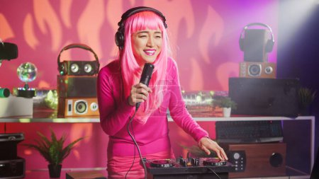 Téléchargez les photos : Musician having fun performing techno music at party in nightclub, using professional audio equipment. Asian performer with pink hair mixing electronic sound using mixer console. Dj concept - en image libre de droit