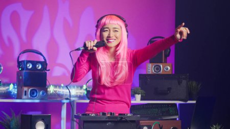 Foto de Musician standing at dj table performing electronic song using professional turntables, enjoying playing music during night time in club. Artist with pink hair doing performance with audio equipment - Imagen libre de derechos