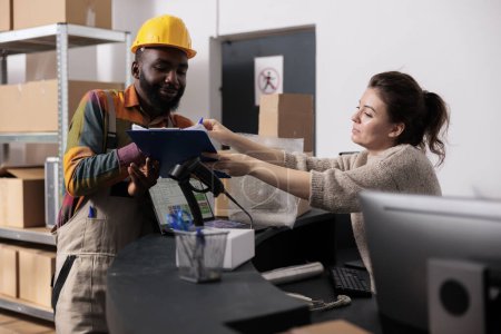 Photo for Stockroom manager putting worker to sign goods checklist, discussing merchandise inventory report in warehouse. Diverse team working at packages delivery, preparing customers orders - Royalty Free Image