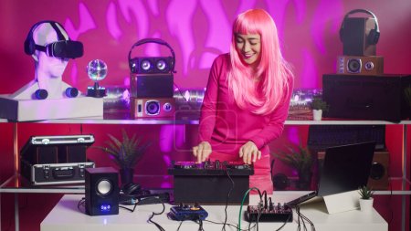 Photo for Artist with pink hair dancing and having fun mixing sound during night time in club, performing eletronic music using professional mixer console. Performer recording album using audio equipment - Royalty Free Image