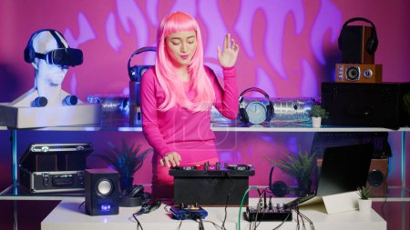 Téléchargez les photos : Artist with pink hair dancing and having fun in nightclub, mixing eletronic sound with techno using professional mixer. Dj performer playing remix using audio equipment, performing at musical event - en image libre de droit