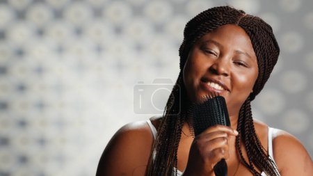 Téléchargez les photos : Jeune femme chantant avec une brosse à cheveux en studio et montrant de la confiance, embrassant les imperfections dans la campagne de soins de la peau. Modèle de beauté se sentant confiant et drôle, favorisant l'acceptation de soi. - en image libre de droit