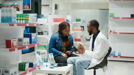 Téléchargez les photos : Médecin afro-américain donnant une bouteille de pilules à une femme, expliquant les médicaments sur ordonnance et les remèdes contre la maladie. pharmacien masculin parlant de vitamines et de suppléments, paquets de médicaments. - en image libre de droit