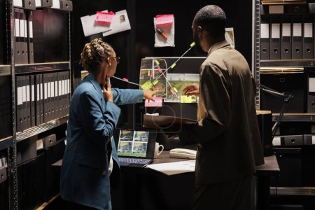 Photo for Police detective partners analyzing clues scheme on detective board. African american woman cop pointing at crime scene and suspect photos connection map, discussing insight with investigator - Royalty Free Image