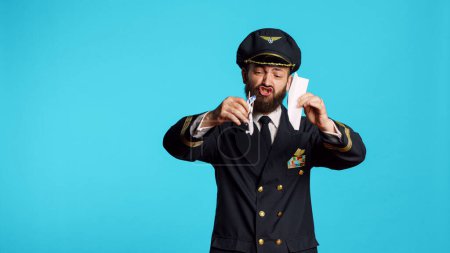 Photo for Aircrew captain playing with paper and toy airplane, having fun with origami and small artificial plane on camera. Professional aviator wearing airline uniform working on commercial flights. - Royalty Free Image