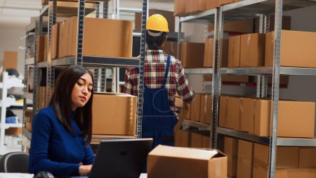 Photo for Young adult analyzing packs of goods in warehouse to help entrepreneur with distribution and business management. Asian team of people working on stock logistics shipment. Handheld shot. - Royalty Free Image