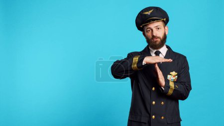 Photo for Commercial pilot doing t shape gesture on camera, asking for break and refusing to work. Professional aircrew captain in uniform showing pause and rejection symbol in studio, air transportation. - Royalty Free Image