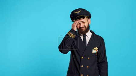 Photo for Sick airplane pilot suffering from headache, being worried about painful migraine and feeling ill. Professional airline captain being unhappy and in pain, feeling pressure rubbing temples. - Royalty Free Image