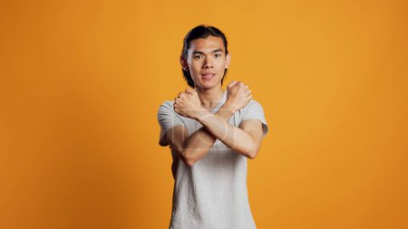 Photo for Asian person showing x shape gesture with hands, expressing refusal and disagreement. Young male model showing no symbol and rejection, refusing to listen over orange backdrop. - Royalty Free Image