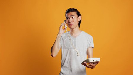 Photo for Young person answering landline phone call on camera, positive guy acting carefree and having remote conversation. Happy smiling man using office telephone to talk, phone with cord. - Royalty Free Image