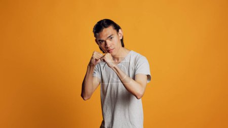 Téléchargez les photos : Furious person clenching fists and acting angry, causing conflict and being aggressive in studio. Young negative guy being violent and punching air, mad man on orange backdrop. - en image libre de droit