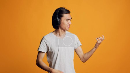 Téléchargez les photos : Modern person playing air guitar and listening to music, having fun with audio headset in studio. Young model feeling cheerful and cool with headphones, singing mp3 song and smiling. - en image libre de droit