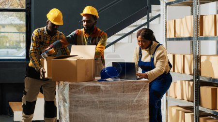 Foto de African american employees trained to use equipment, working in packaging department with skills. Team of people using merchandise boxes packs to ship products, stock distribution. - Imagen libre de derechos