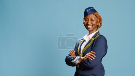 Téléchargez les photos : Femme confiante et joyeuse qui travaille comme hôtesse de l'air, porte l'uniforme d'aviation et pose pour le succès. Hôtesse de l'air souriante positive se préparant pour le vol commercial, industrie du vol. - en image libre de droit