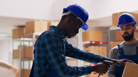 Photo for Two employees using scanner and digital tablet for stock logistics and inventory, scanning barcodes for boxes of products in storage room depot. Young men in overalls working in warehouse. - Royalty Free Image