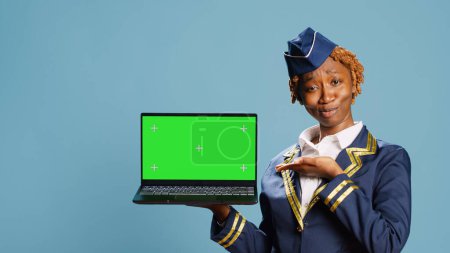 Photo for Air hostess holding laptop with green screen display, pointing st blank chroma key template on pc. Aircrew member using computer with isolated copyspace screen, mockup background. - Royalty Free Image