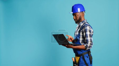 Photo for Modern constructor using laptop to find inspiration for building project, browsing online and making calculations or measurements on camera. Construction worker holding wireless pc to work. - Royalty Free Image