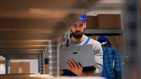 Photo for Caucasian worker holding laptop with inventory list, checking merchandise stock and planning order shipment. Male manager holding pc to do quality control for goods. Handheld shot. - Royalty Free Image