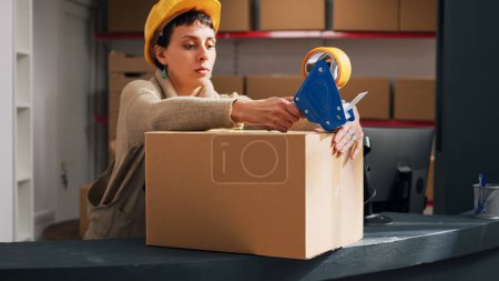 Photo for Depot worker sealing off packages of stock goods, using adhesive tape to prepare merchandise order for distribution. Young man packing storage room products in cardboard boxes. - Royalty Free Image