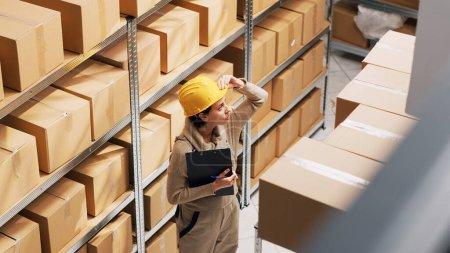 Photo for Female employee counting number of packages in depot storage room, checking products on shelves. Young woman working on stock logistics, doing inventory before products shipment. - Royalty Free Image