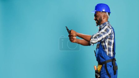 Photo for Construction worker clamping something with wrench in studio, using carpentry instrument for building and renovation work. Male constructor working with spanner mechanical tool. - Royalty Free Image