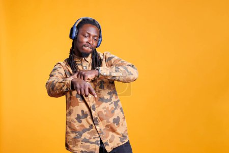 Photo for African american young adult enjoying music playlist during leisure activity, dancing and having fun in studio over yellow background. Playful man wearing headset listening song, enjoying free time - Royalty Free Image