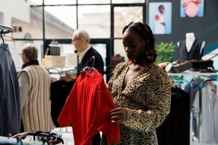 Photo for Pregnant client shopping for stylish pregnancy clothes in clothing store, checking t shirt fabric. African american woman buying fashionable merchandise for maternity in modern showroom - Royalty Free Image