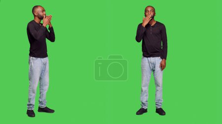 Foto de Hombre afroamericano enviando besos al aire en cámara, posando con la cara besada en pantalla verde de cuerpo completo. Adulto joven siendo romántico en el estudio y haciendo gesto coqueto, reacción optimista. - Imagen libre de derechos