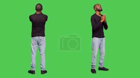 Foto de Joven hombre espiritual orando a Jesús en el estudio, tomándose de la mano en una oración y pidiendo perdón. Persona religiosa con creencia, adulto optimista en el fondo de pantalla verde de cuerpo completo. - Imagen libre de derechos