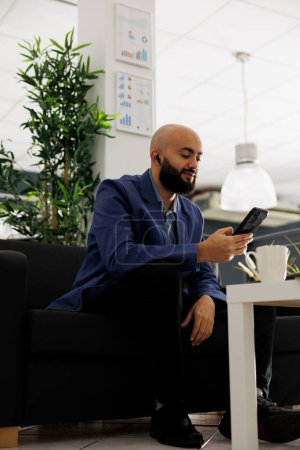 Foto de Empleado de la compañía discutiendo estrategia de negocio en videoconferencia smartphone. Árabe profesional sentado en el sofá y tener comunicación en línea con el equipo remoto en la oficina - Imagen libre de derechos