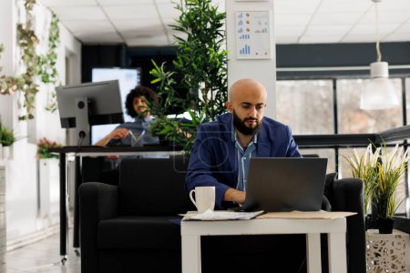 Entrepreneur arabe d'affaires travaillant à la gestion des données marketing sur ordinateur portable dans un bureau moderne à espace ouvert. Démarrer gestionnaire exécutif résoudre tâche de travail tout en tapant sur l'ordinateur