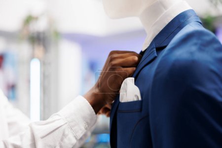 Foto de Moda boutique de trabajadores afroamericanos manos ajustando chaqueta formal en el modelo, mostrando ropa para la venta. Centro comercial asistente de fijación traje masculino en maniquí de cerca - Imagen libre de derechos