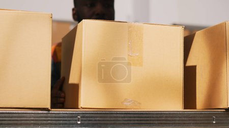 Photo for Male worker organizing packs in depot, moving products in cardboard boxes for shipping and delivery. Employee carrying packages in storage room, doing quality control. Handheld shot. Close up. - Royalty Free Image