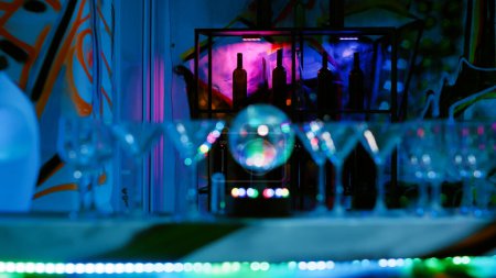 Photo for Empty bar with alcohol drinks and disco ball, glasses in the nightclub used for partying and entertainment. Modern club with electronic music and dance floor with spotlights. Close up. - Royalty Free Image