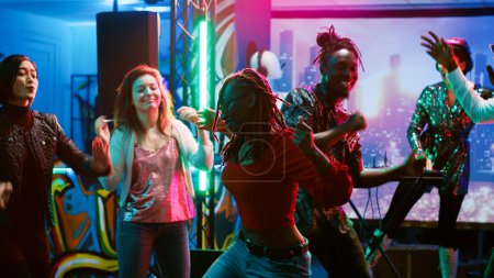 Foto de Mujer afroamericana de fiesta en el club, disfrutando de la vida nocturna con amigos en la pista de baile. Grupo de jóvenes que se divierten sintiéndose felices en el club nocturno, escuchando música estéreo. Trípode tiro. - Imagen libre de derechos