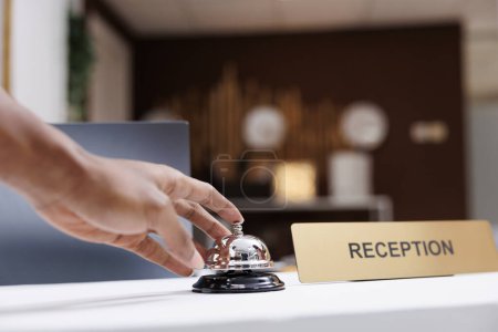 Photo for Guest ringing service bell at front desk, waiting to receive assistance from hotel staff at reception counter. Male tourist calling out receptionist, looking for accommodation. Close up. - Royalty Free Image