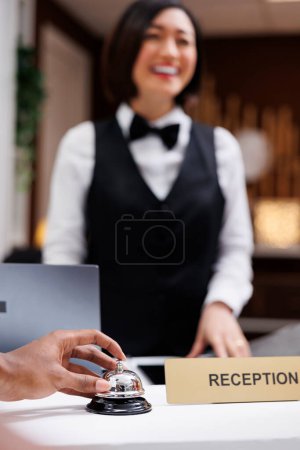 Photo for Person ringing bell at hotel reception with front desk staff working on check in and registration process. Young man using service bell in resort lobby, receptionist welcoming people. Close up. - Royalty Free Image