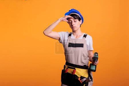 Photo for Tired young contractor with drilling gun feeling sleepy and fatigued, falling asleep at renovating project work. Female builder being exhausted with burnout and holding drill screw tool. - Royalty Free Image